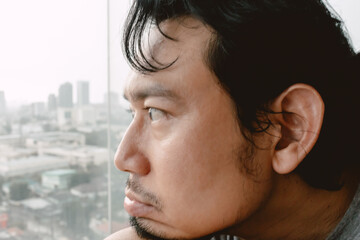 Introvert lonely asian man sitting hugging his knees looking out.