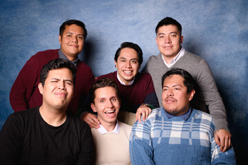 Group of 6 men in sweater on blue background in 90's yearbook style. Posing comically as a family