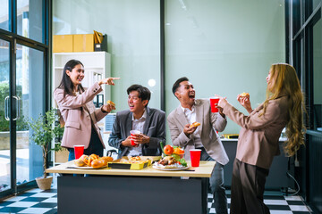 Four Asian friends, two men and two women, celebrate in an office party. They enjoy a fun-filled with food, drinks, and laughter, bonding over teamwork and friendship.
