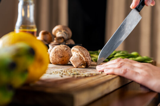 person preparing dinner in the kitchen, swiss brown mushroom on a wooden cutting board, healthy food concept