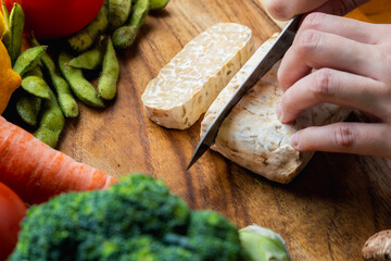 slice raw tempeh block with other vegetables ingredients on a wooden board