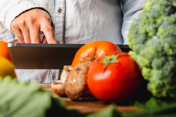 A woman is looking for a recipe on a tablet while preparing fresh vegetables on a wooden cutting board, healthy food concept