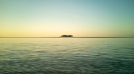Sunrise beach and black silhouette motion blur. Nature background sea, golden evening sky and blurred island.