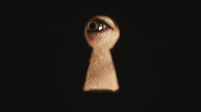 Male blue eye looking through the keyhole. The concept of voyeurism, curiosity, Stalker, surveillance and security