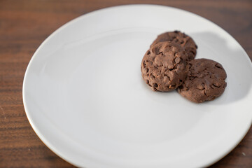 tres galletas de chocolate con chispas de chocolate sobre plato blanco con espacio para texto