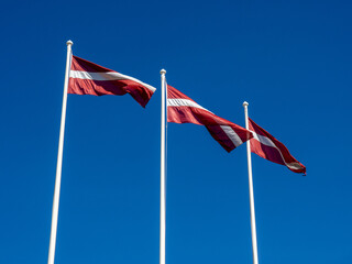 Three Latvian flags on white masts and blue sky. The day of the proclamation of Latvia s independence on November 18. The day of restoration of national independence on May 4