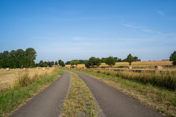 Country road between farm fields, hay bales and trees in summer