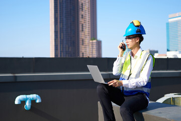 Engineer working on laptop computer and talking on walkie talkie at construction site