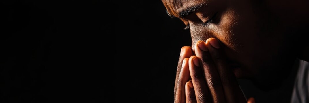Close-up portrait of an African American man praying with his hands clasped together, his eyes closed in contemplation and devotion. This image captures the essence of faith, hope, and spirituality. - Powered by Adobe