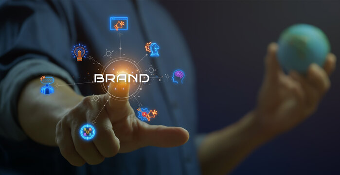 Businessman shows glowing neon line of BRAND concept with icons of innovation, advertising, customer, target market, strategy, marketing and awareness on virtual screen.