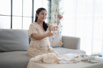 Pregnant asian woman getting ready for the maternity hospital preparing and planning baby clothes for new baby of pregnancy packing baby stuff on bed.