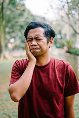 Obraz premium Southeast Asian man holding his cheek, showing discomfort from a toothache