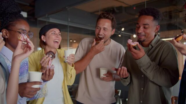 Laughing co-workers enjoy lunch eating donuts with coffee