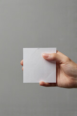 A hand holds a blank sheet of paper on a gray background