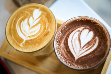 Two cups with latte art are standing on the wooden tray