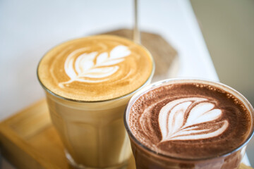 Two glasses with latte art on wooden tray are standing on white table