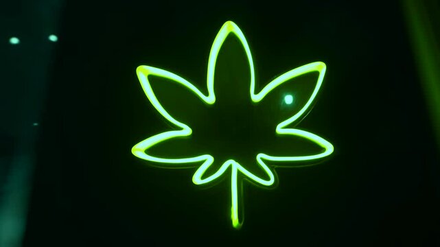 Long exposure abstract bad trip intoxication effect of green neon marijuana leaf logo glowing on the wall of cannabis shop on the street at night. Legalization for medical and recreational use
