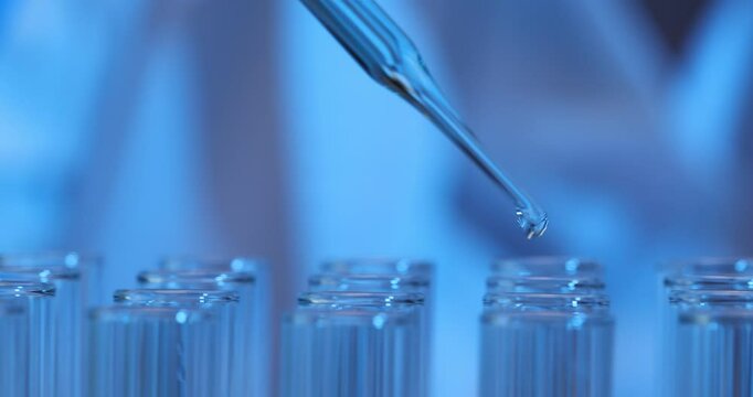 Scientist uses a dropper to add liquid to glass test tubes in laboratory
