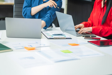Two Asian business woman work at a desk, discussing business strategies, marketing, plans.They...