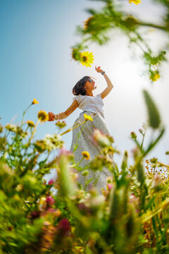 Summer mood. a young and cheerful girl posing against a background of blue sky and flowers. A beautiful girl dances among flowers. girl dancing among flowers.
