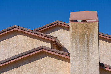 A tall stucco chimney shows discoloration and weathering, rising beside a multi-layered roof with terracotta tiles
