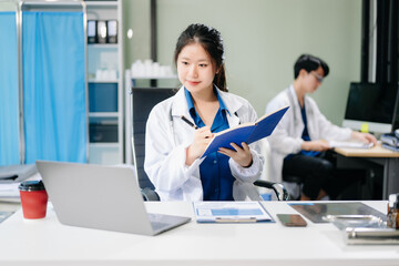Fototapeta premium Confident young asian female doctor in white medical uniform sit at desk working on computer.