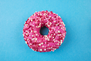 Donut with pink icing and sprinkles on a blue background. Top view, close-up.