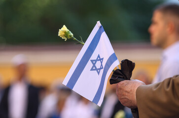 Details with the hands of a man holding the Israeli flag and a flower during a ceremony...