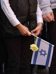 Obraz premium Details with the hands of a boy holding the Israeli flag and a flower during a ceremony commemorating the October 2023 attacks
