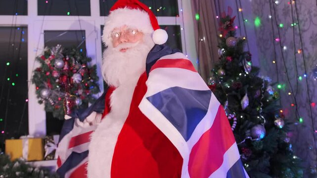 Santa Claus supporter of British team with England flag among Christmas decorations with flickering garlands of festive Xmas tree. Close up. Merry Xmas party.