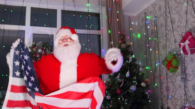 Santa Claus dances with USA flag next to Xmas tree with twinkling garlands, close up. Happy New Year and Merry Christmas.