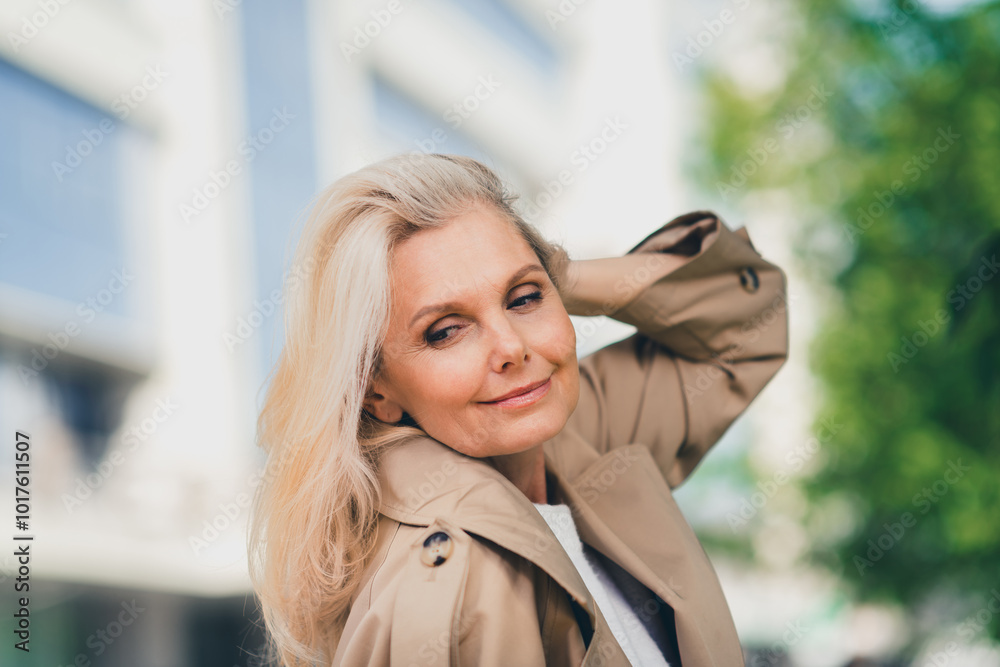 Wall mural Portrait of positive cheerful happy retired woman walk smile spring touch hair weekend wear beige coat enjoy outdoors outside park street