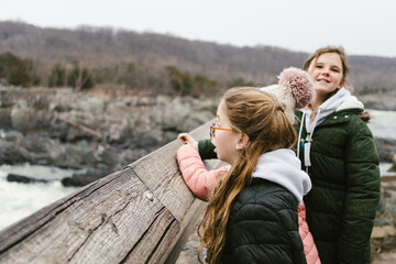 Tween girls overlook a river in coats in fall in mountain valley