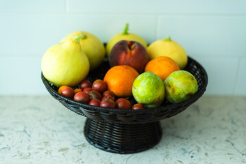 A basket of assorted fresh fruits,squash, tomatoes, and peaches.