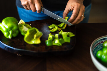 Close-up of women chopping green bell peppers on a wooden board.