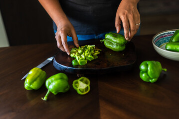 Women Slicing green bell peppers on a dark wooden kitchen surface.