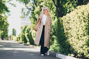 Full length photo of cheerful happy retired woman walking smile spring good mood weekend wear beige coat enjoy outdoors outside park street