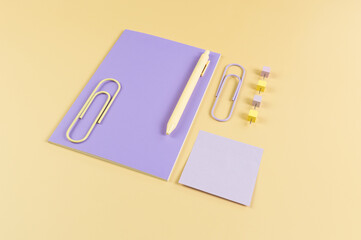 Top view of purple notebook on yellow background. Sticky note, paperclips, pen and pins. School, office wallpaper. Flat lay, copy space.