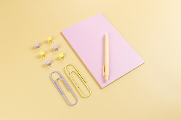 Top view of pink notebook on yellow background. Paperclips, pen and pins. School, office wallpaper. Flat lay, copy space.