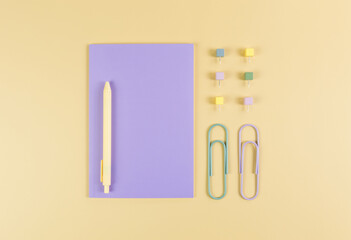 Top view of purple notebook on yellow background. Paperclips, pen and pins. School, office wallpaper. Flat lay, copy space.