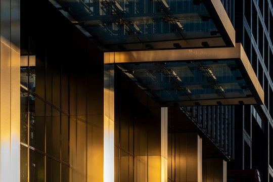 The sleek exterior of a modern glass building reflects golden rays of sunset, creating stunning contrasts of light and shadow on its smooth surfaces.
