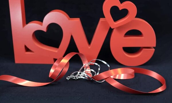 Bijou en or expos&eacute; dans une vitrine de bijouterie pour la Saint-Valentin, accompagn&eacute; d'une sculpture rouge formant le mot anglais "love" et d'un bolduc pour un emballage cadeau, sur fond noir
