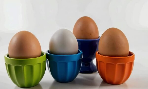 Quatre &oelig;ufs &agrave; la coque dans des coquetiers color&eacute;s, avec un &oelig;uf blanc distinctif, sur fond clair