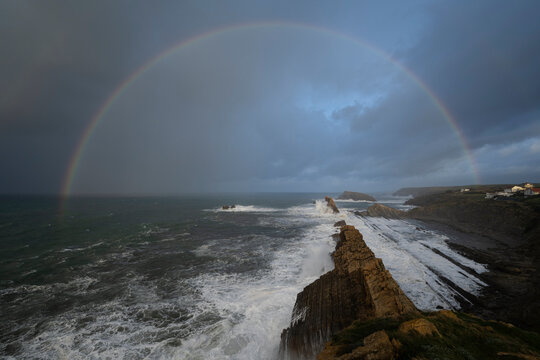 Rainbow over rocky coastline at Playa De La Arnia, Spain