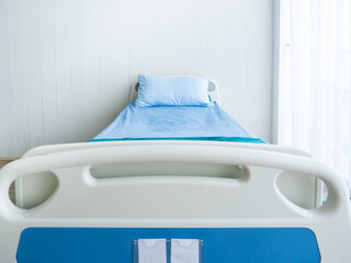 Front view of an empty hospital bed featuring blue bedding and a pillow, placed in a bright,...