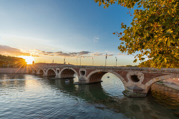 Obraz premium Golden sunset over the Garonne river and Pont Neuf in downtown Toulouse. This arch bridge is considered a masterpiece of the Renaissance. The bridge is not symmetrical.