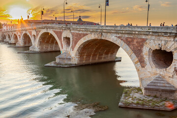 Golden sunset over the Garonne river and Pont Neuf in downtown Toulouse. This arch bridge is considered a masterpiece of the Renaissance. The bridge is not symmetrical.