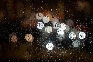 Raindrops on a window at night. Rain drops on glass window with night city lights on background, close-up © Gecko Studio