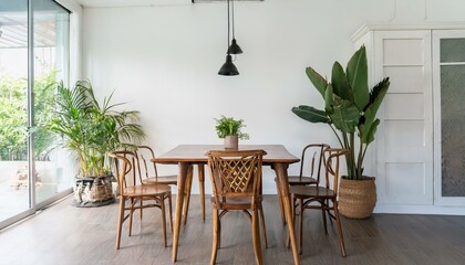 Fototapeta premium Vintage interior design of kitchen space with small table against white wall with simple chairs and plant decorations. Minimalistic concept of kitchen space.