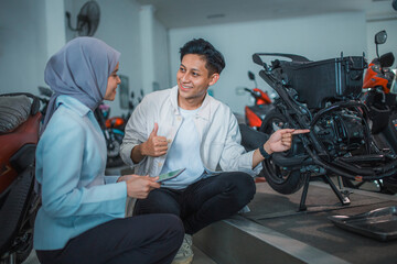 man with thumbs up and veiled saleswoman checking the underframe of a motorcycle at a showroom